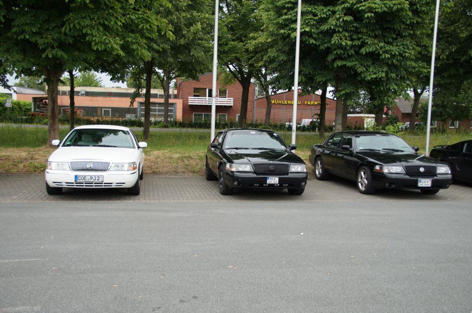 Three sedans parked in a lot, one white and two black.