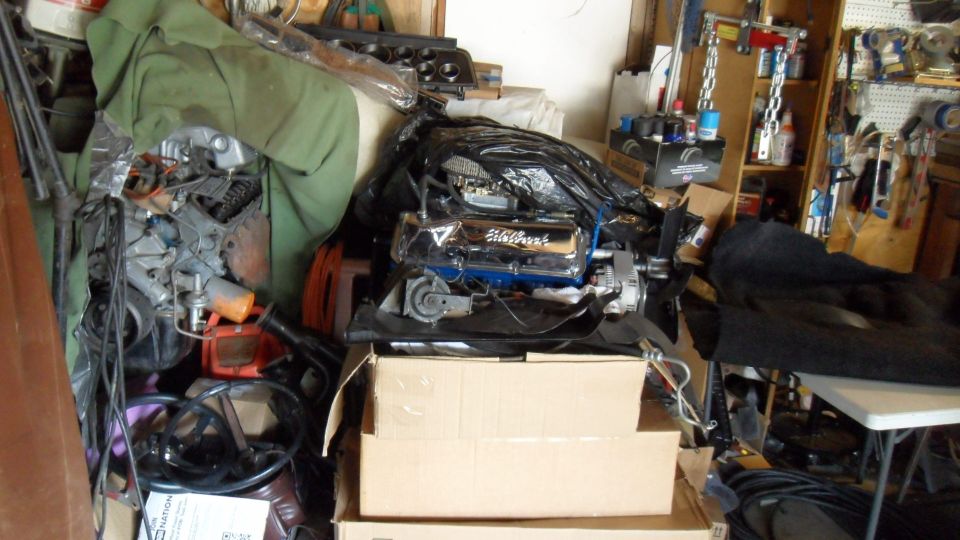 Engine with chrome valve covers in a garage, covered by plastic and tarp.