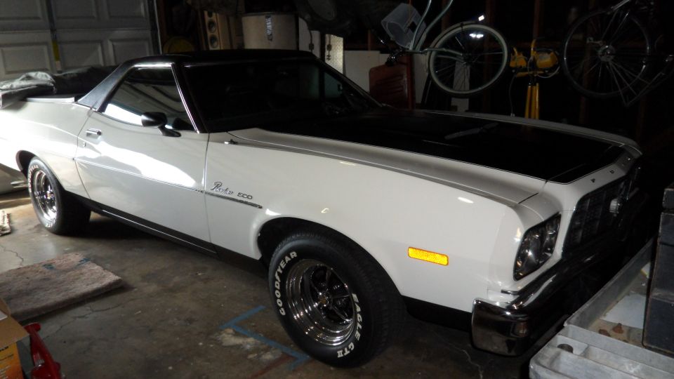 1972 Ford Ranchero with black top and hood, chrome wheels, in a garage.