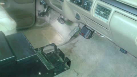 1996 Ford Bronco - The interior of a vehicle's driver's side footwell is shown, with the dashboard, pedals, and floor mats visible. A black metal bracket with…