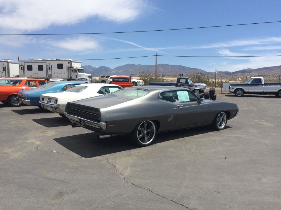 Photo of a gray Ford Torino parked at a dealer lot near mountains