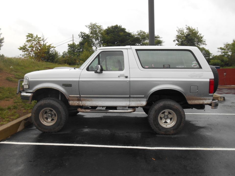 Side view of a silver and gray 1994 Ford Bronco parked on a wet surface.