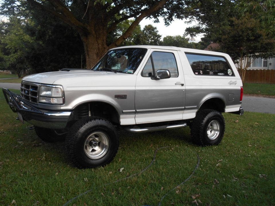 Lifted 1994 Ford Bronco, white and gray, with bull bar and aftermarket wheels, parked on grass.