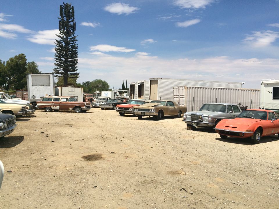 Outdoor lot full of classic cars and trailers under blue sky