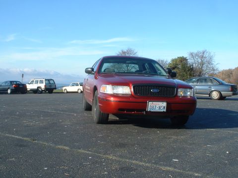 1999 Ford Crown Victoria - Red Ford Crown Victoria parked in a lot with other vehicles and a clear blue sky.