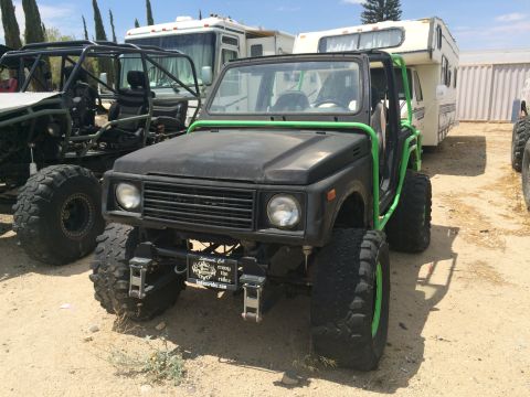 1968 Ford Mustang - Photograph of a modified black Suzuki Samurai 4x4 with a green roll cage parked in a dirt yard.