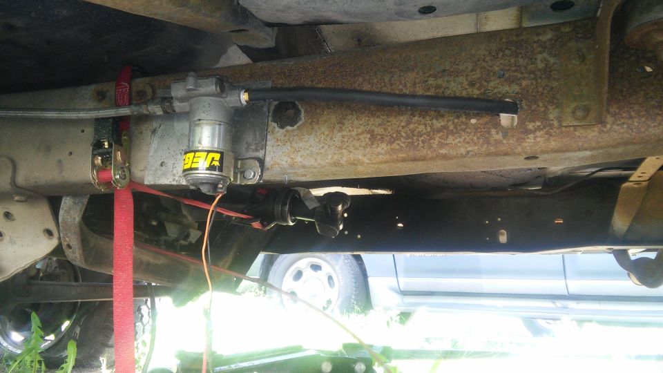 Underneath vehicle view of JEG fuel filter and fuel line secured with ratchet straps.