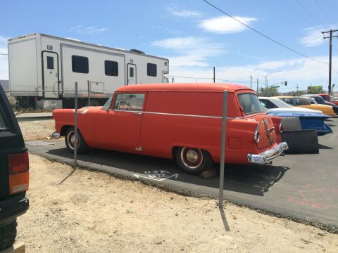1968 Ford Mustang - Photograph of an orange vintage 1950s sedan-delivery panel car parked beside a fence.