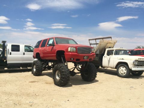 1968 Ford Mustang - Photograph of a red lifted GMC SUV on oversized tires among other vehicles in a dirt yard.