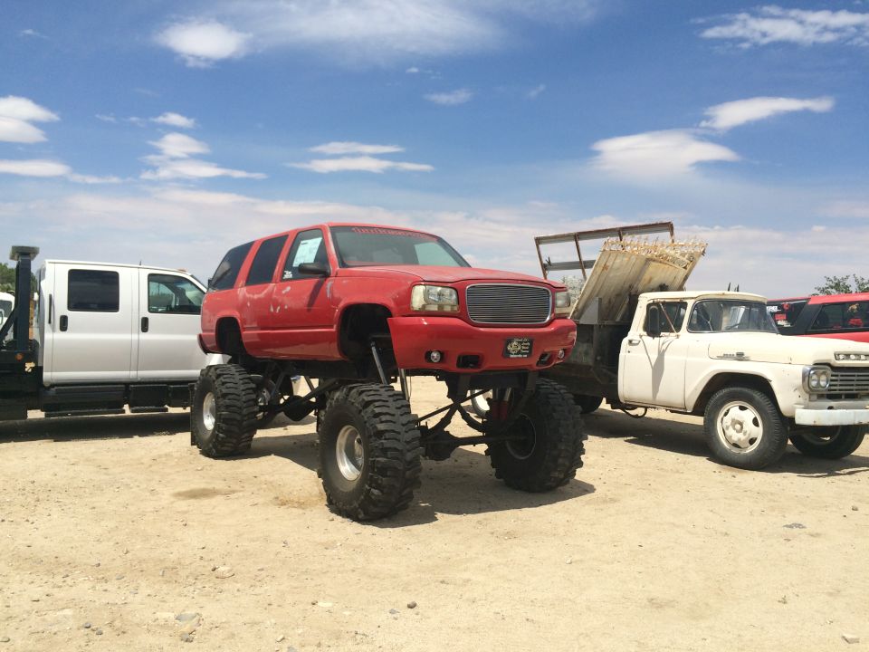 Photo of a red lifted GMC SUV on large tires in a vehicle yard