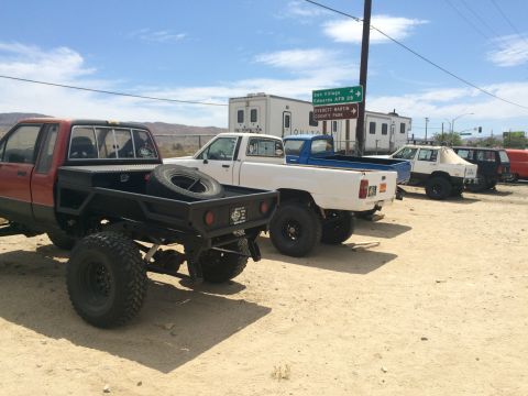 1968 Ford Mustang - Photograph of several lifted flatbed and pickup trucks parked in a desert lot near highway signs.