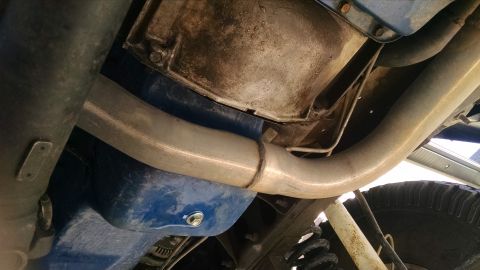 1979 Ford F-150 - The underside of a vehicle shows a blue oil pan with a drain plug and a silver exhaust pipe running above it. The engine or transmission ca…