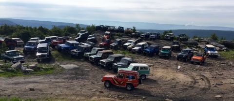 1974 Ford Bronco - A large group of vintage Ford Broncos are parked on a rocky, elevated terrain with a scenic mountain landscape in the background. The vehic…