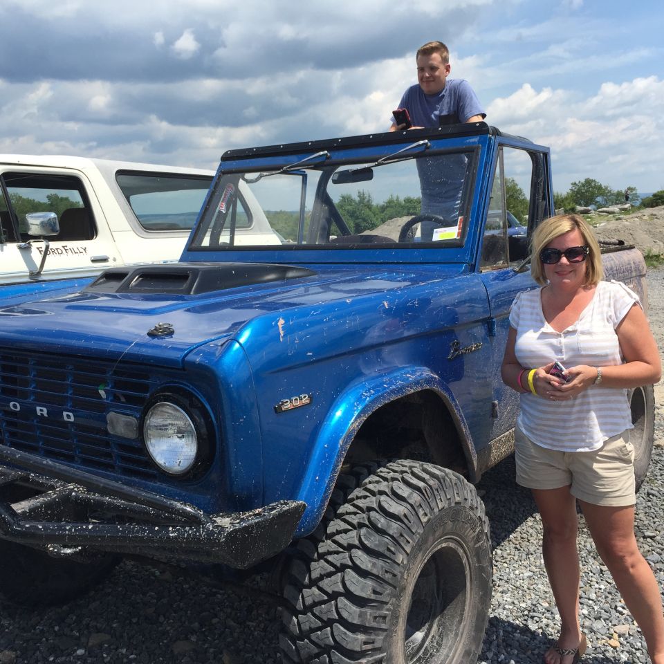 Blue 1974 Ford Bronco with a woman standing next to it and a man in the driver's seat.