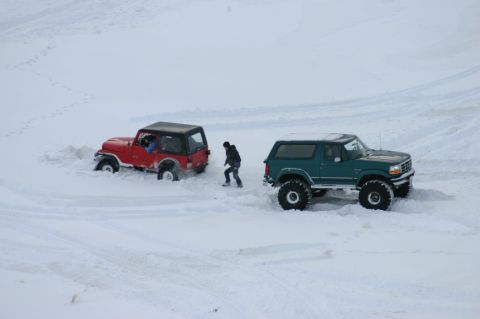 1996 Ford Bronco - Two SUVs are stuck in deep snow, with a person walking between them.