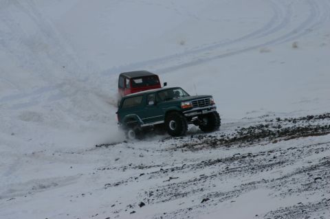 1996 Ford Bronco - A green 1996 Ford Bronco navigates a snowy terrain, with another vehicle following behind.