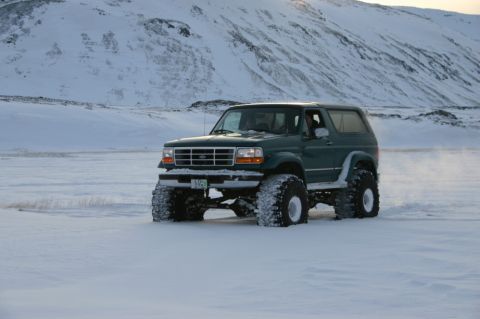 1996 Ford Bronco - A green 1996 Ford Bronco equipped with large off-road tires navigates a snowy landscape.