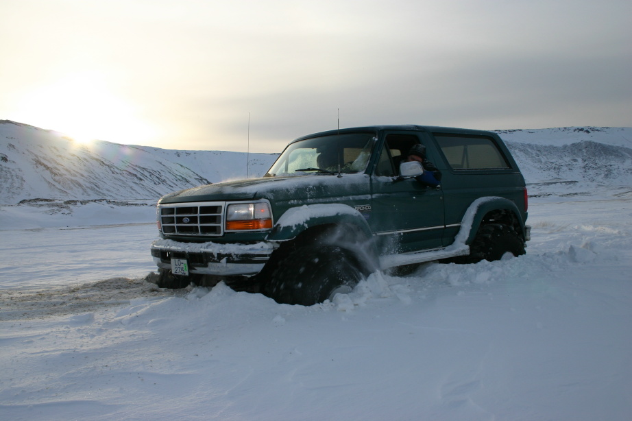 Dark green Ford Bronco SUV driving through deep snow at sunset