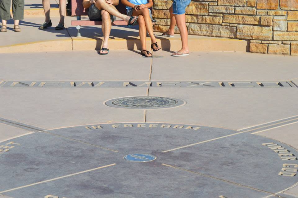 Four Corners Monument marker on the ground with people standing around it.
