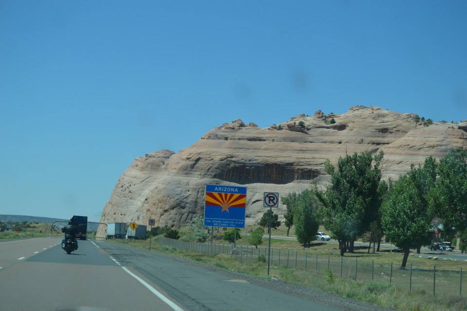 Motorcycle on highway in Arizona with rock formation and welcome sign.