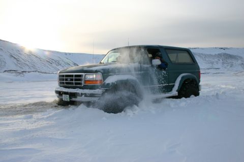 1996 Ford Bronco - A green Ford Bronco navigates through deep snow, sending powder flying.