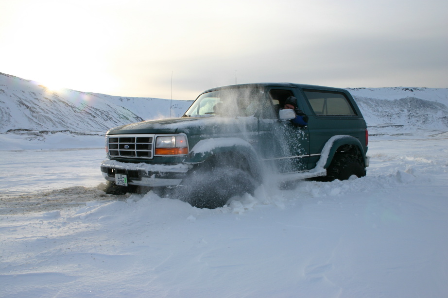 Dark green Ford Bronco driving through deep snow, spraying powder in a snowy landscape