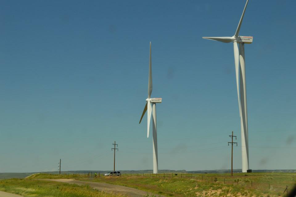 Wind turbines in a field with a road and a white SUV.