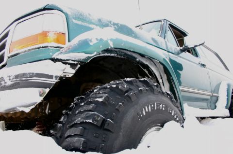 1996 Ford Bronco - Green SUV partially buried in snow, showing a large off-road tire.