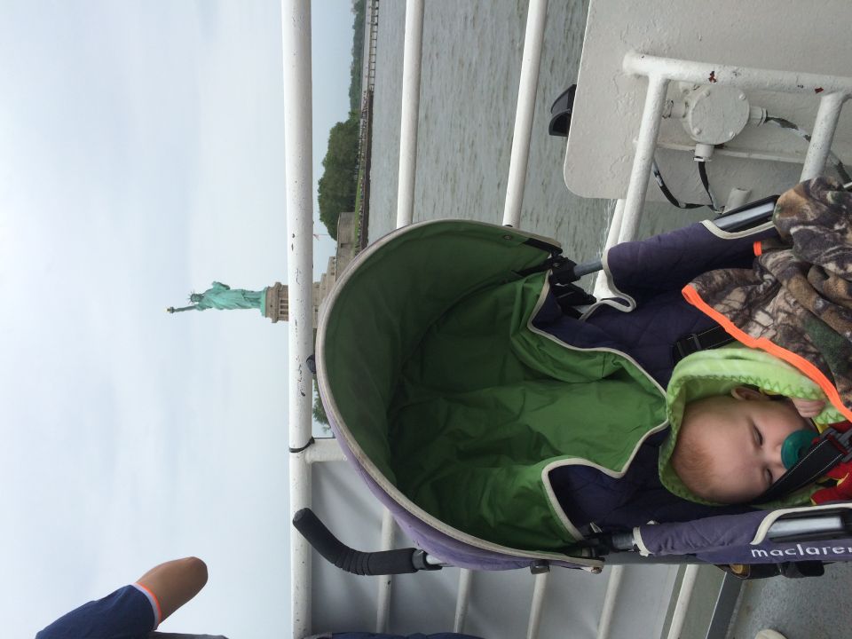 Baby in a stroller on a boat with the Statue of Liberty in the background