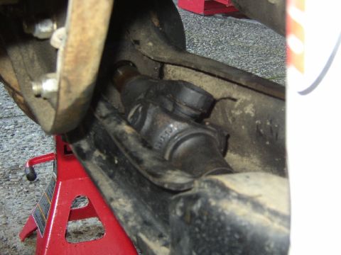 1989 Ford Bronco - Underside view of a vehicle's front axle assembly, showing the driveshaft and related components supported by a red jack.