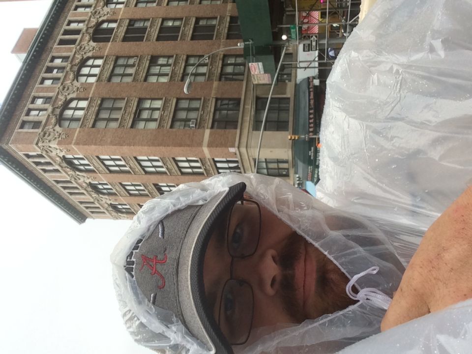 Man in a rain poncho selfie in front of a brick building