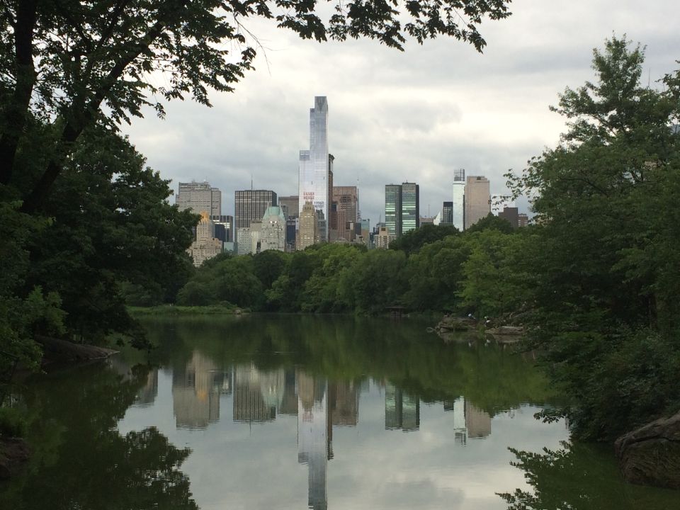 Manhattan skyline reflected in a calm Central Park lake framed by trees