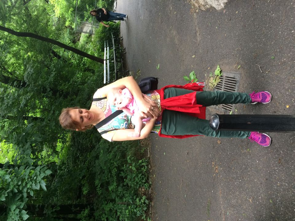 Woman holding an infant standing on a path in a wooded Central Park area