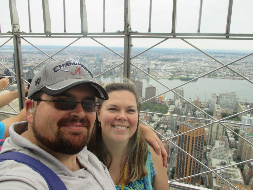 Couple at Empire State Building observation deck with New York City skyline behind them