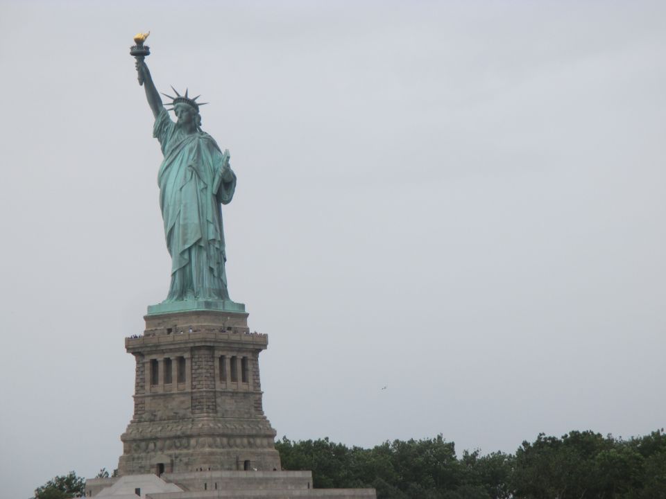 Statue of Liberty against a cloudy sky with trees in the foreground