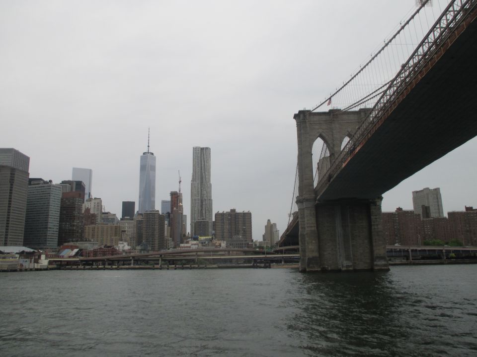 Brooklyn Bridge and New York City skyline under an overcast sky, viewed from the water