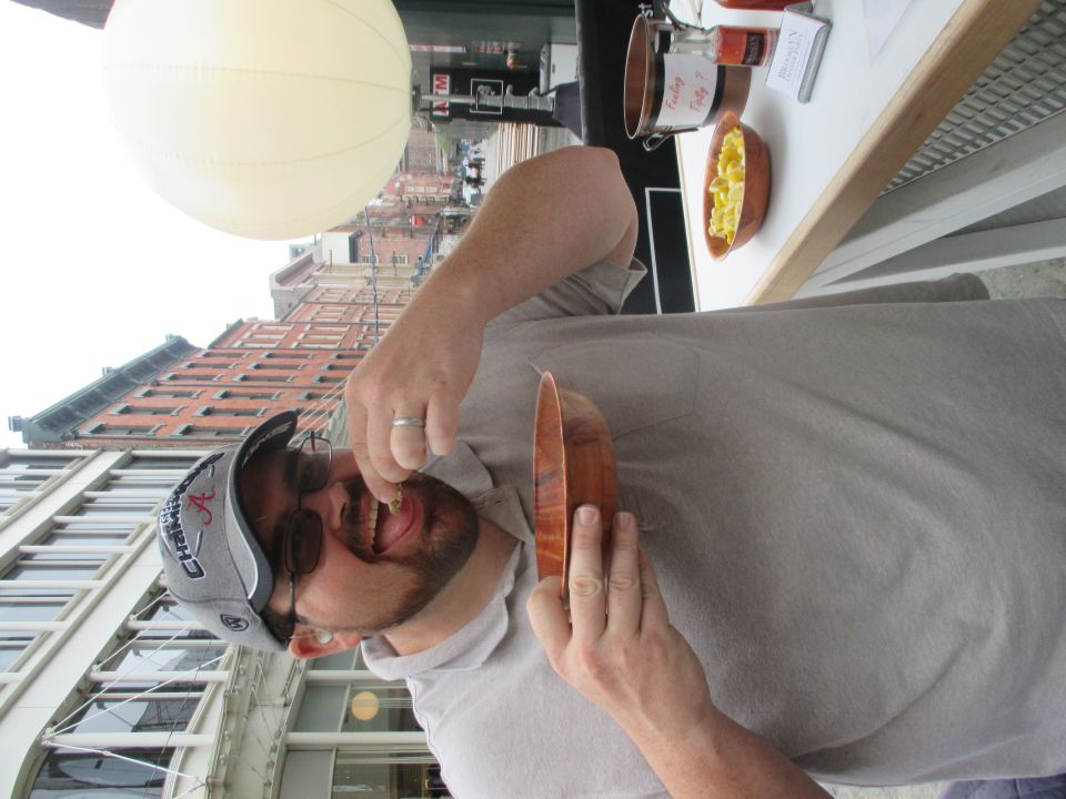 Man eating from a wooden bowl with buildings in the background