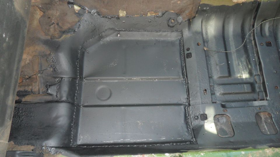 Close-up of a vehicle's floor pan with new metal welded in and painted black