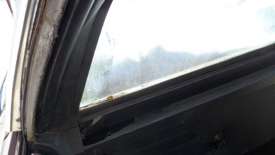 Close-up of a car's interior window frame and seal, showing wear and tear