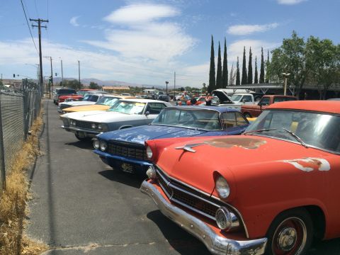 1968 Ford Mustang - A line of classic cars are parked in a lot under a bright blue sky with scattered clouds.