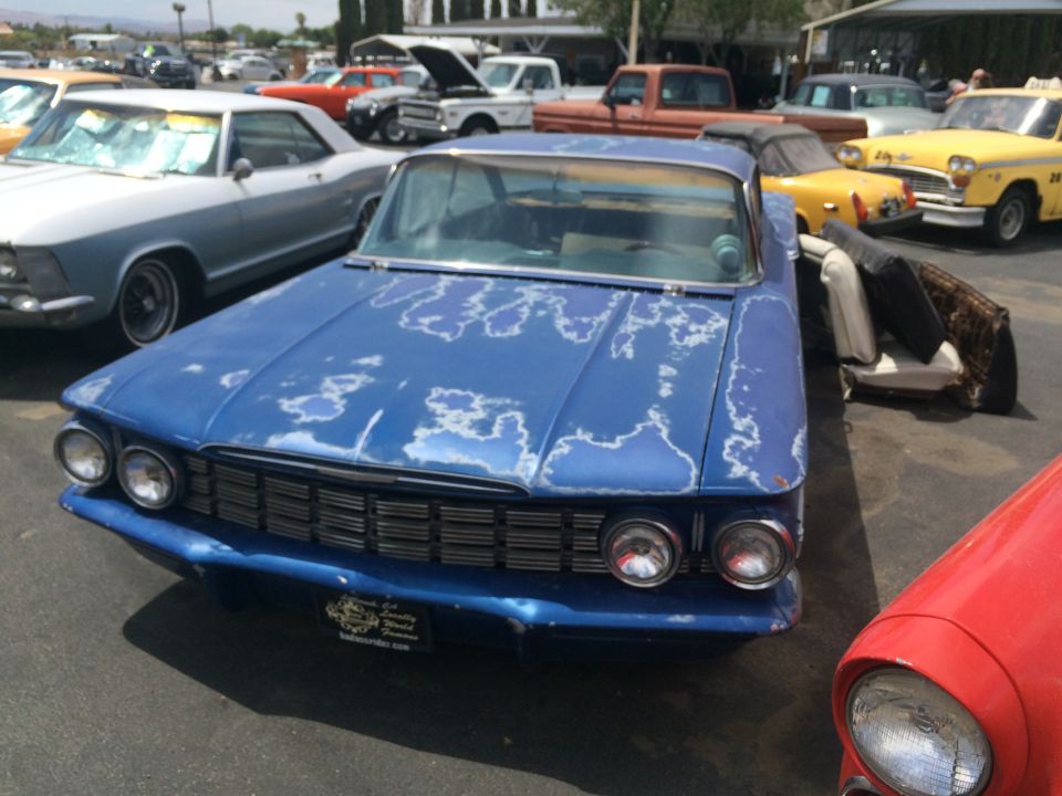 Blue sedan with peeling paint, parked outside with other cars. A car seat is visible next to it