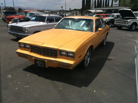 1968 Ford Mustang - This yellow coupe, likely from the early 1980s, is parked in a lot with other vehicles.