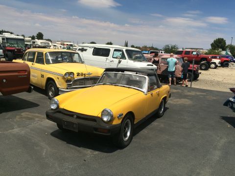 1968 Ford Mustang - A yellow convertible sports car is parked in a lot alongside a yellow taxi and other vehicles under a partly cloudy sky.