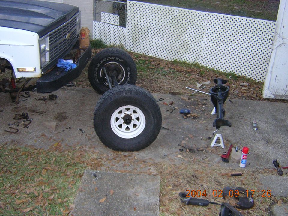 Front of a white and black truck with its front wheels removed, showing a chrome grille and bumper