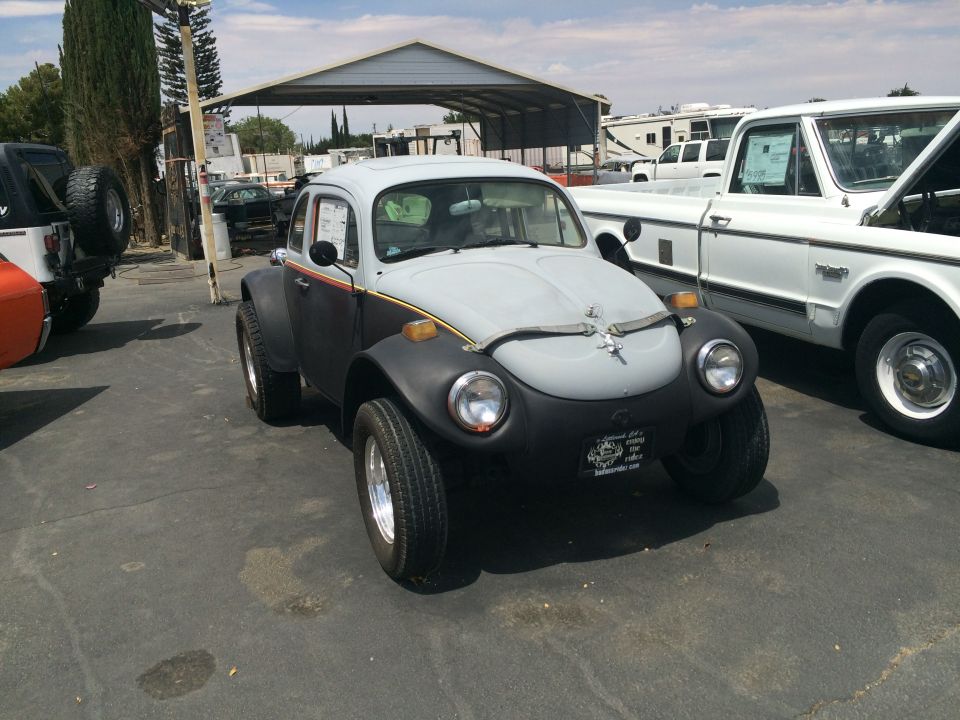 Modified VW Beetle with wide fenders and off-road tires parked next to a white pickup truck