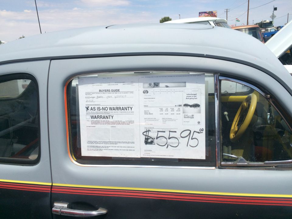 Gray car side view with price sticker $55.95 on window and yellow steering wheel
