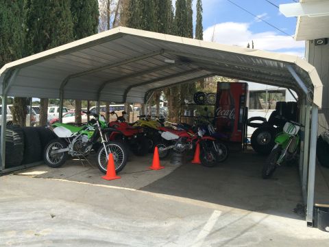 1968 Ford Mustang - Several dirt bikes and ATVs are stored under a metal carport alongside stacks of tires and a vintage Coca-Cola vending machine.
