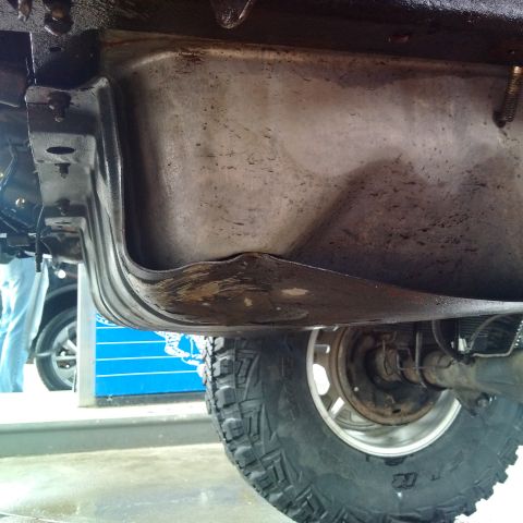 1978 Ford Bronco - Undercarriage view of a vehicle, focusing on a dented fuel tank and a tire.