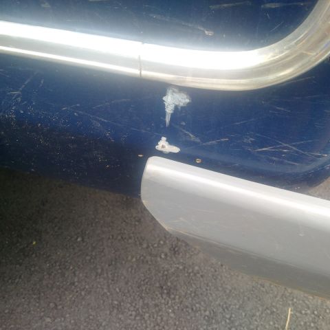 1978 Ford Bronco - Close-up of a blue vehicle's exterior, revealing scratches and damage on the body panel and chrome trim.