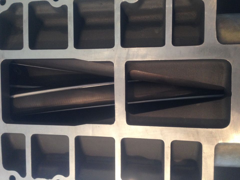 Close-up of a supercharger intake manifold with internal passages visible. Supermotors.net logo in lower right